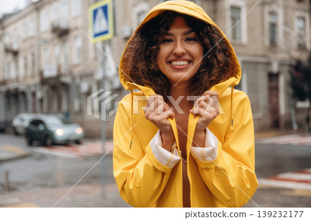 In yellow raincoat, standing and smiling. Happy young woman in the city during the rain 139232177