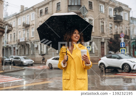 Hot drink is in the paper cup. Happy young woman in the city during the rain Hot drink is in the paper cup. Happy young woman in the city during the rain 139232195