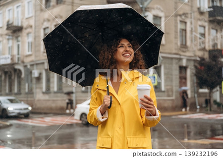 Hot drink is in the paper cup. Happy young woman in the city during the rain Hot drink is in the paper cup. Happy young woman in the city during the rain 139232196