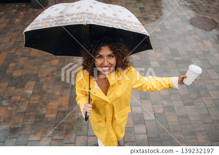 Top view of woman that is standing with an umbrella and a cup of coffee in a rainy city, on the cobblestones 139232197