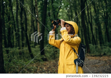 Binoculars is in hands. Young woman enjoying nature in the forest under the rain Binoculars is in hands. Young woman enjoying nature in the forest under the rain 139232223