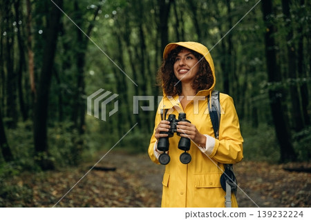 Binoculars is in hands. Young woman enjoying nature in the forest under the rain Binoculars is in hands. Young woman enjoying nature in the forest under the rain 139232224