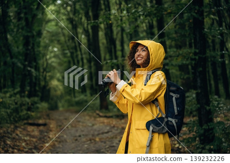 The binoculars, conception of discovery. Young woman enjoying nature in the forest under the rain 139232226