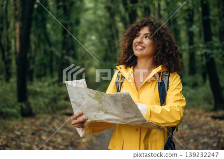 Paper map is in hands, looking at location. Young woman enjoying nature in the forest under the rain Paper map is in hands, looking at location. Young woman enjoying nature in the forest under the rain 139232247