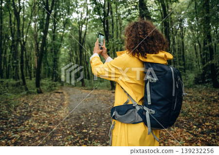 Making photos by using smartphone. Young woman enjoying nature in the forest under the rain Making photos by using smartphone. Young woman enjoying nature in the forest under the rain 139232256