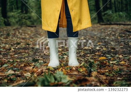 Having a walk. Close up view of woman legs, in rainy forest, yellow raincoat and rubber boots Having a walk. Close up view of woman legs, in rainy forest, yellow raincoat and rubber boots 139232273