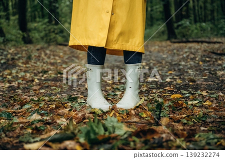 Having a walk. Close up view of woman legs, in rainy forest, yellow raincoat and rubber boots Having a walk. Close up view of woman legs, in rainy forest, yellow raincoat and rubber boots 139232274