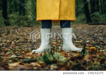 Having a walk. Close up view of woman legs, in rainy forest, yellow raincoat and rubber boots Having a walk. Close up view of woman legs, in rainy forest, yellow raincoat and rubber boots 139232275
