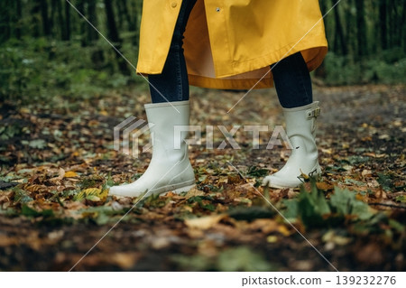 Having a walk. Close up view of woman legs, in rainy forest, yellow raincoat and rubber boots Having a walk. Close up view of woman legs, in rainy forest, yellow raincoat and rubber boots 139232276