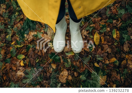 Close up view of woman legs, in rainy forest, yellow raincoat and rubber boots Close up view of woman legs, in rainy forest, yellow raincoat and rubber boots 139232278