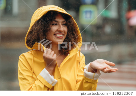 In yellow raincoat, standing and smiling. Happy young woman in the city during the rain In yellow raincoat, standing and smiling. Happy young woman in the city during the rain 139232307