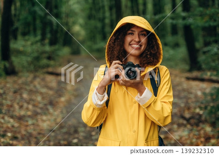 Photographer is with camera. Young woman enjoying nature in the forest under the rain Photographer is with camera. Young woman enjoying nature in the forest under the rain 139232310