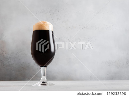 Glass of fresh cold dark stout beer with foam on light table background. Glass of fresh cold dark stout beer with foam on light table background. 139232898
