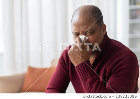 Mature African American man blowing nose into tissue at home 139233399
