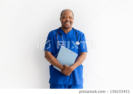 Cheerful mature African American male doctor in blue scrubs holding clipboard Cheerful mature African American male doctor in blue scrubs holding clipboard 139233451