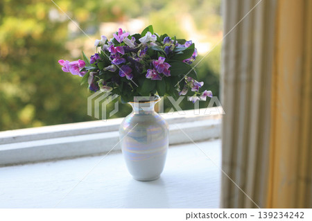 Bouquet of purple flowers in a small iridescent vase on a windowsill Bouquet of purple flowers in a small iridescent vase on a windowsill 139234242
