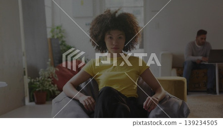 Sitting woman wearing yellow T-shirt on beanbag chair at home while friend reclining with laptop Sitting woman wearing yellow T-shirt on beanbag chair at home while friend reclining with laptop 139234505