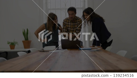 Reviewing documents colleagues in business casual leaning over laptop at meeting table, with pens Reviewing documents colleagues in business casual leaning over laptop at meeting table, with pens 139234516