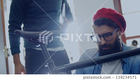 Kneeling mechanic wearing red beanie adjusting seat post in workshop, with bicycle frame and saddle Kneeling mechanic wearing red beanie adjusting seat post in workshop, with bicycle frame and saddle 139234571