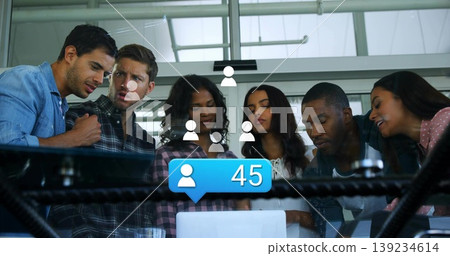 Six coworkers leaning over laptop on desk in office, showing social media icons, blue 45 bubble Six coworkers leaning over laptop on desk in office, showing social media icons, blue 45 bubble 139234614