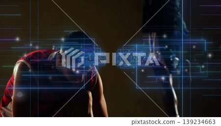 Crouched male athlete sprinting in dark studio with standing partner, projecting blue AR overlays Crouched male athlete sprinting in dark studio with standing partner, projecting blue AR overlays 139234663