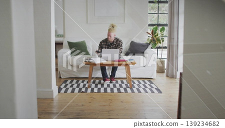 Man wearing plaid shirt typing on laptop and checking smartphone on coffee table in living room Man wearing plaid shirt typing on laptop and checking smartphone on coffee table in living room 139234682
