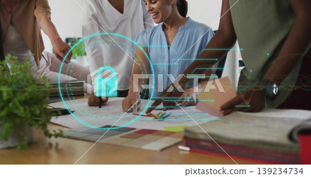 Four women collaborating over blueprints around table in studio, with holographic lock overlay 139234734