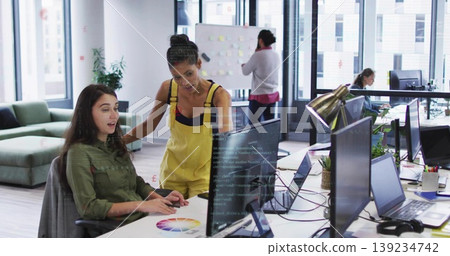 Collaborating female designers pointing at monitors in open-plan office, with printed color wheel Collaborating female designers pointing at monitors in open-plan office, with printed color wheel 139234742