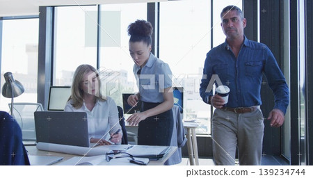 Collaborating professionals reviewing documents, pointing at blueprint near laptop in modern office Collaborating professionals reviewing documents, pointing at blueprint near laptop in modern office 139234744