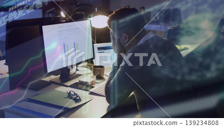 Adult man wearing shirt under sweater viewing charts on screens and tablet in office, with lamp Adult man wearing shirt under sweater viewing charts on screens and tablet in office, with lamp 139234808