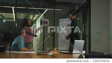 Professional woman highlighting printed chart against glass wall in conference room, with laptop Professional woman highlighting printed chart against glass wall in conference room, with laptop 139234839
