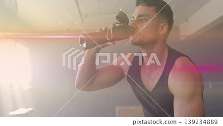 Drinking from steel water bottle, sunglasses on cap, man in sleeveless top at gym, copy space Drinking from steel water bottle, sunglasses on cap, man in sleeveless top at gym, copy space 139234889