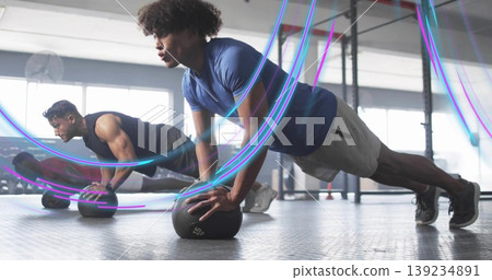 Doing push-ups man in athletic clothes balancing on medicine ball in gym room with pull-up rig Doing push-ups man in athletic clothes balancing on medicine ball in gym room with pull-up rig 139234891