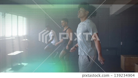 Three men skipping jump ropes in fitness studio, with large windows plyo boxes weight bench Three men skipping jump ropes in fitness studio, with large windows plyo boxes weight bench 139234904
