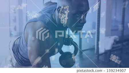 Man in sportswear performing one-arm kettlebell row in gym weight area, with racks and bars, towel Man in sportswear performing one-arm kettlebell row in gym weight area, with racks and bars, towel 139234907