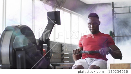 Rowing man wearing red shirt on rowing machine with digital monitor at gym, copy space Rowing man wearing red shirt on rowing machine with digital monitor at gym, copy space 139234916