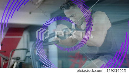 Pedaling man in workout clothes on air bike at gym, with purple overlays and red racks Pedaling man in workout clothes on air bike at gym, with purple overlays and red racks 139234925