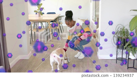 Crouching Black woman feeding cream-colored dog in modern dining area, stainless steel bowl Crouching Black woman feeding cream-colored dog in modern dining area, stainless steel bowl 139234937