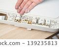 Hand replacing clear silicone button membrane on a white home printer control panel, revealing the exposed circuit board, buttons and ribbon cable, maintenance and electronics repair at a workbench. 139235813