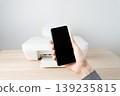 Person holds a smartphone in front of a printer on a wooden desk, wireless mobile printing and connectivity for a modern home office, highlighting convenience, productivity and simple workflow. 139235815
