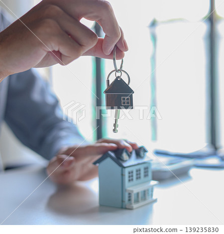 Hand giving key with house-shaped keychain. Concept for buying, selling, renting or leasing a new home. 139235830