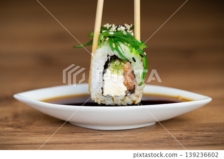 delicious traditional Japanese sushi and rolls on a plate holding chopsticks delicious traditional Japanese sushi and rolls on a plate holding chopsticks 139236602