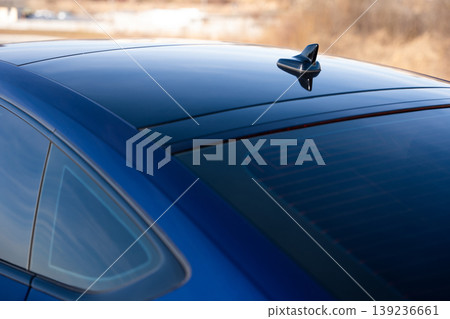 Close-up of the roof, shark fin antenna, and rear window of a dark blue sedan Close-up of the roof, shark fin antenna, and rear window of a dark blue sedan 139236661