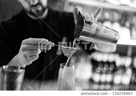 Professional bartender straining a cocktail into a glass Professional bartender straining a cocktail into a glass 139236867