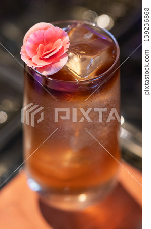 Iced amber cocktail garnished with a pink flower Iced amber cocktail garnished with a pink flower 139236868