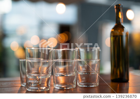Empty drinking glasses stacked on a wooden table with a wine bottle 139236870