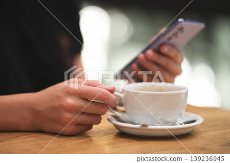 Person holding a smartphone and a cup of coffee in a cafe 139236945