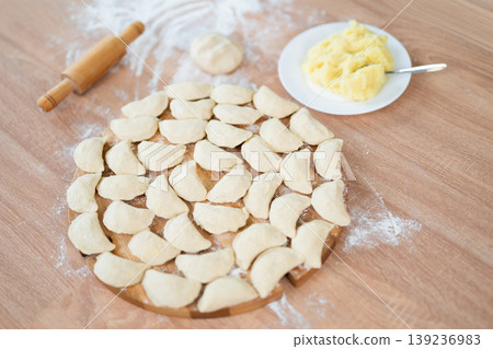 Homemade dumplings with potato filling on a wooden board next to a rolling pin 139236983