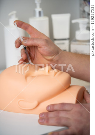 a cosmetologist trains to inject a cosmetic syringe into the face of a rubber mannequin a cosmetologist trains to inject a cosmetic syringe into the face of a rubber mannequin 139237535