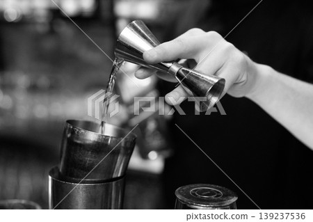 Bartender pouring liquid from a jigger into a shaker Bartender pouring liquid from a jigger into a shaker 139237536